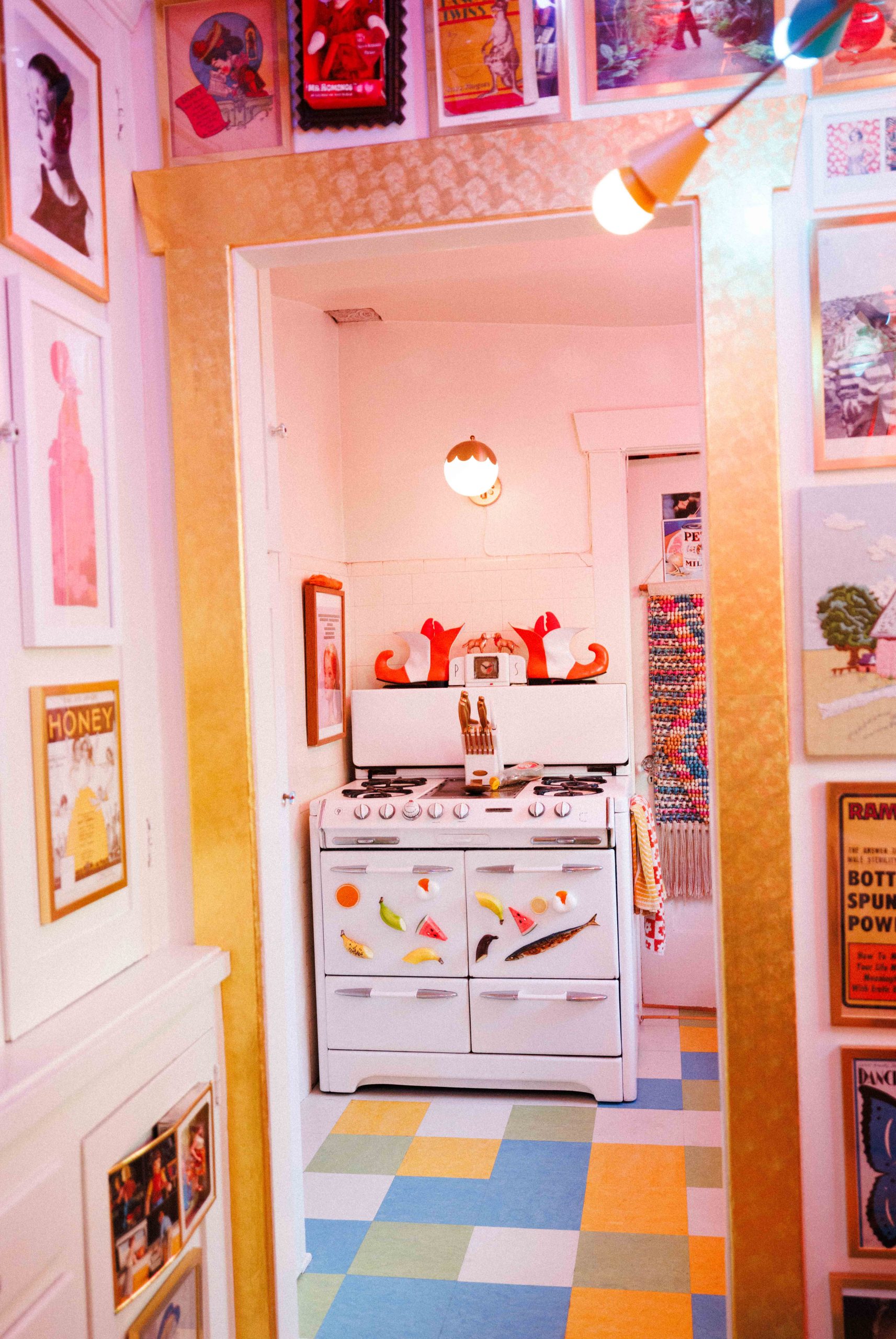 A view through a pink, art-filled doorway into a kitchen with a multicolored floor.