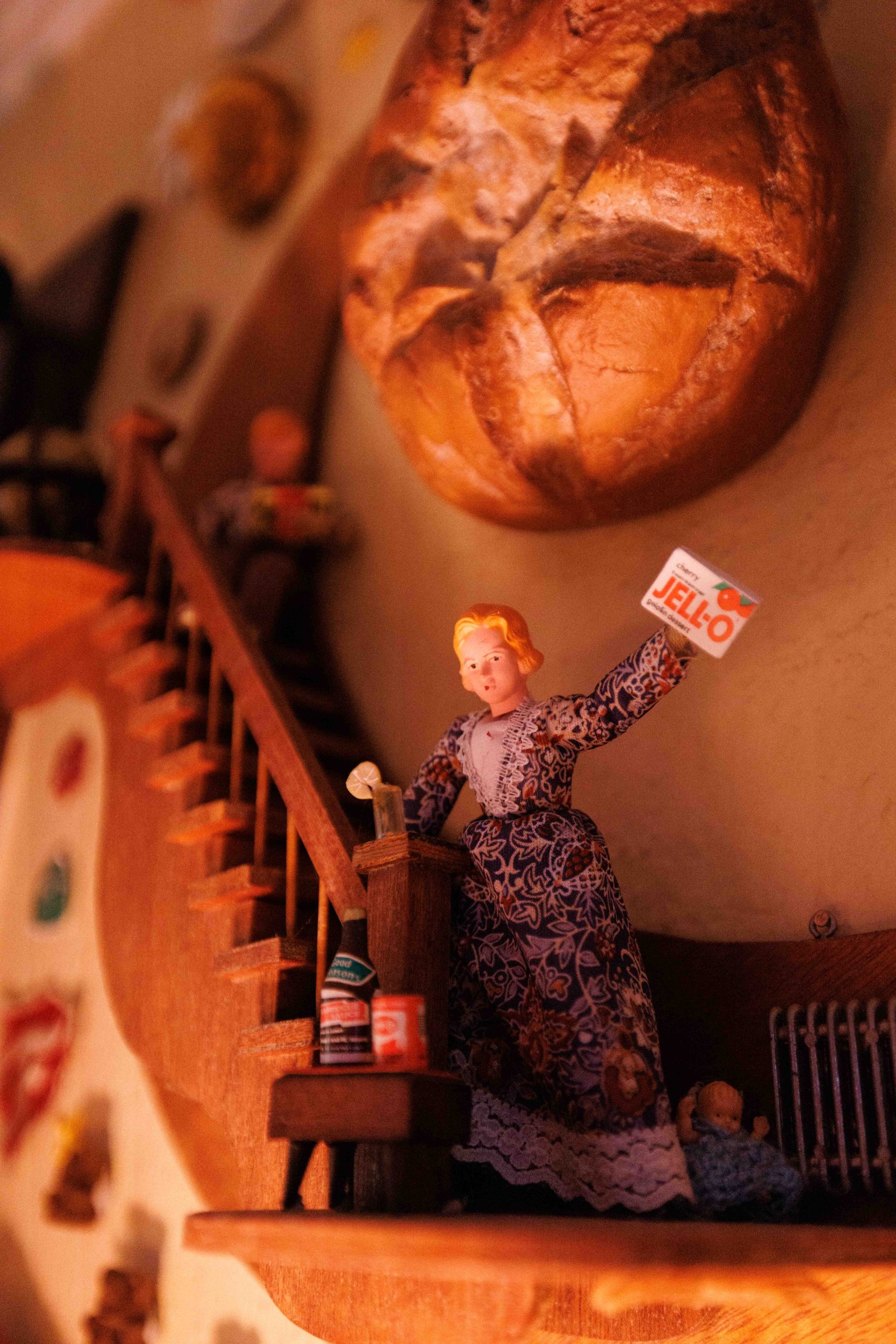 A miniature figure holds an EXIT sign on a tiny staircase beneath a bread-shaped wall ornament.