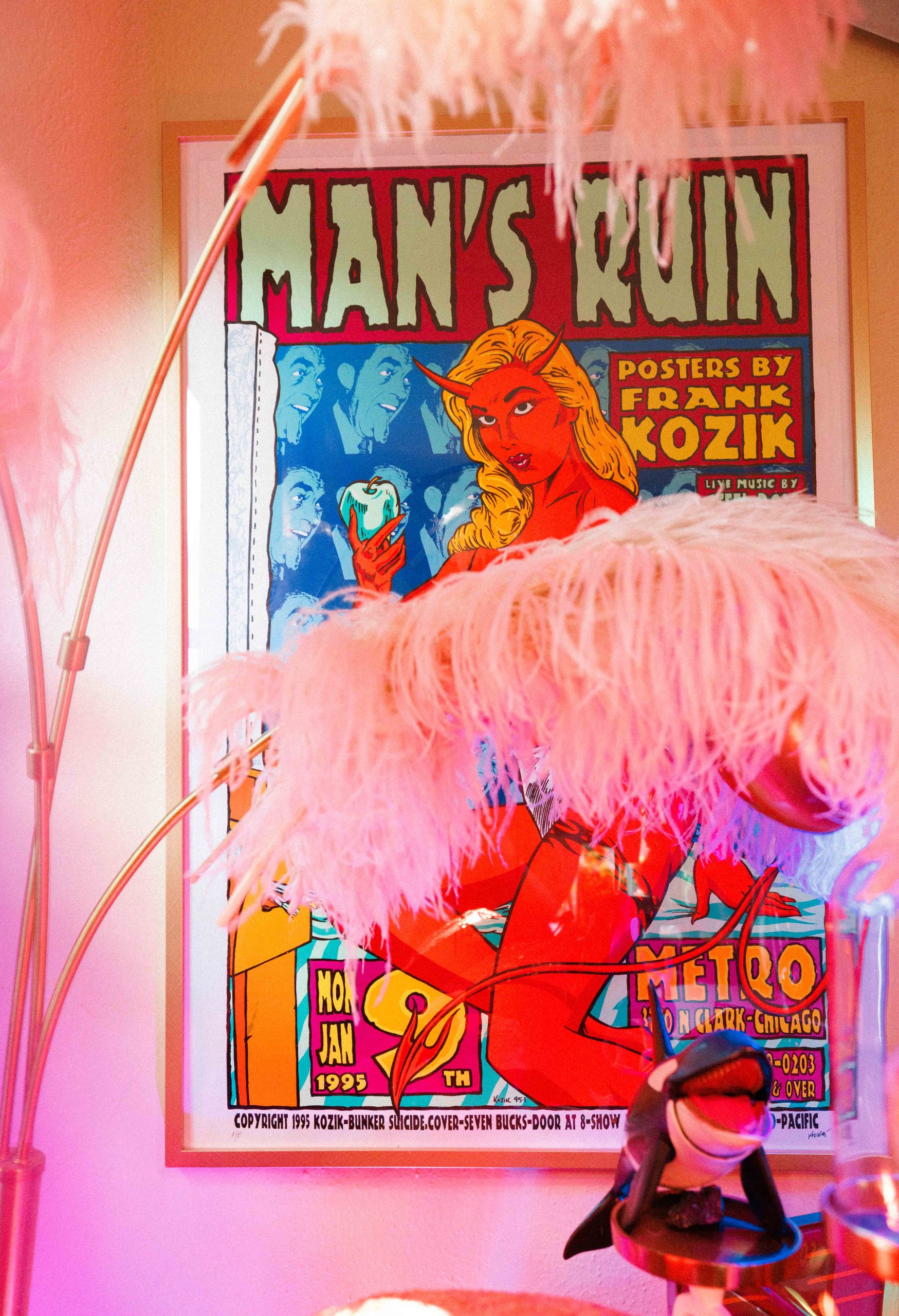 Pink feathers hang in front of a framed Man’s Ruin poster.