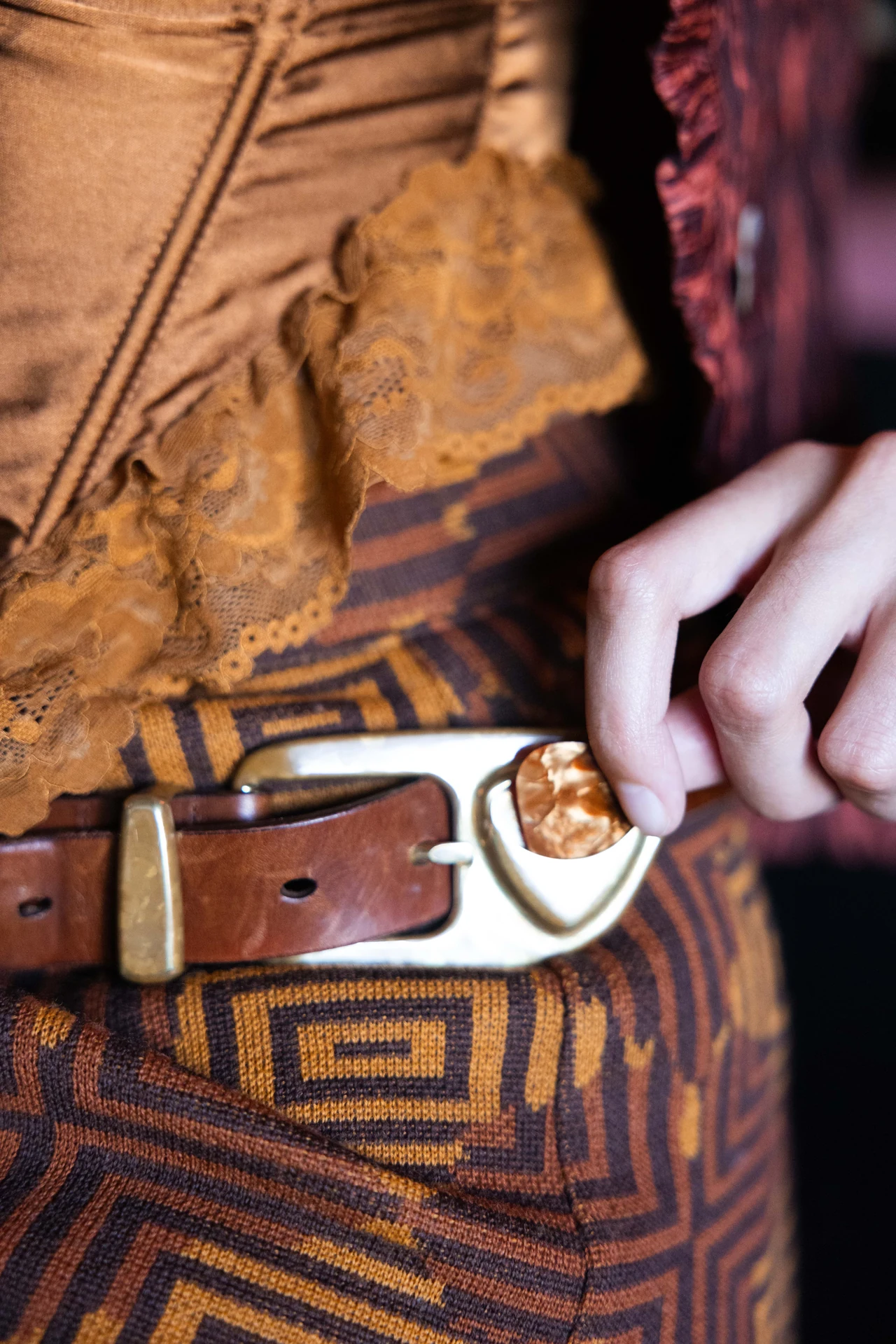 Close-up of a hand reaching for a guitar pick held in the belt buckle.