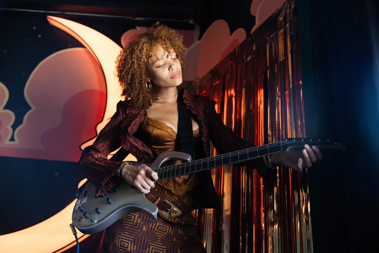 Portrait with an electric guitar against metallic fringe and a painted moon backdrop.