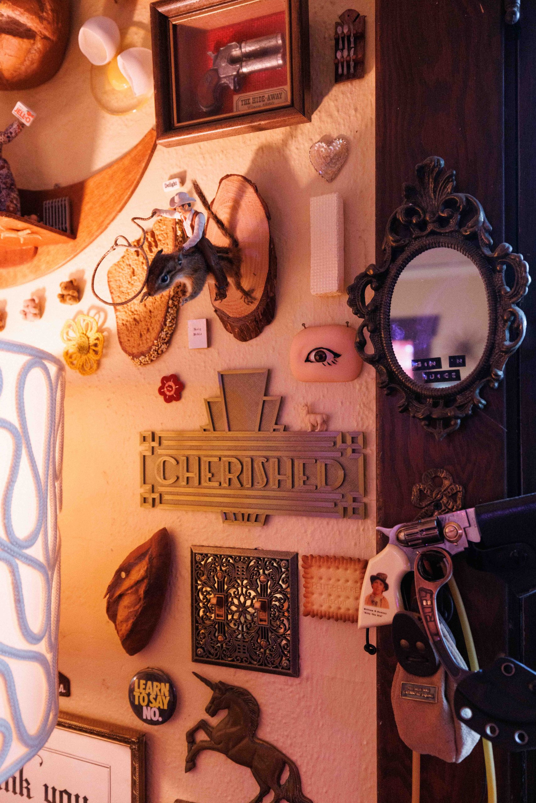 A wall crowded with small mirrors, framed pictures, ornaments, and a plaque reading Cherished.