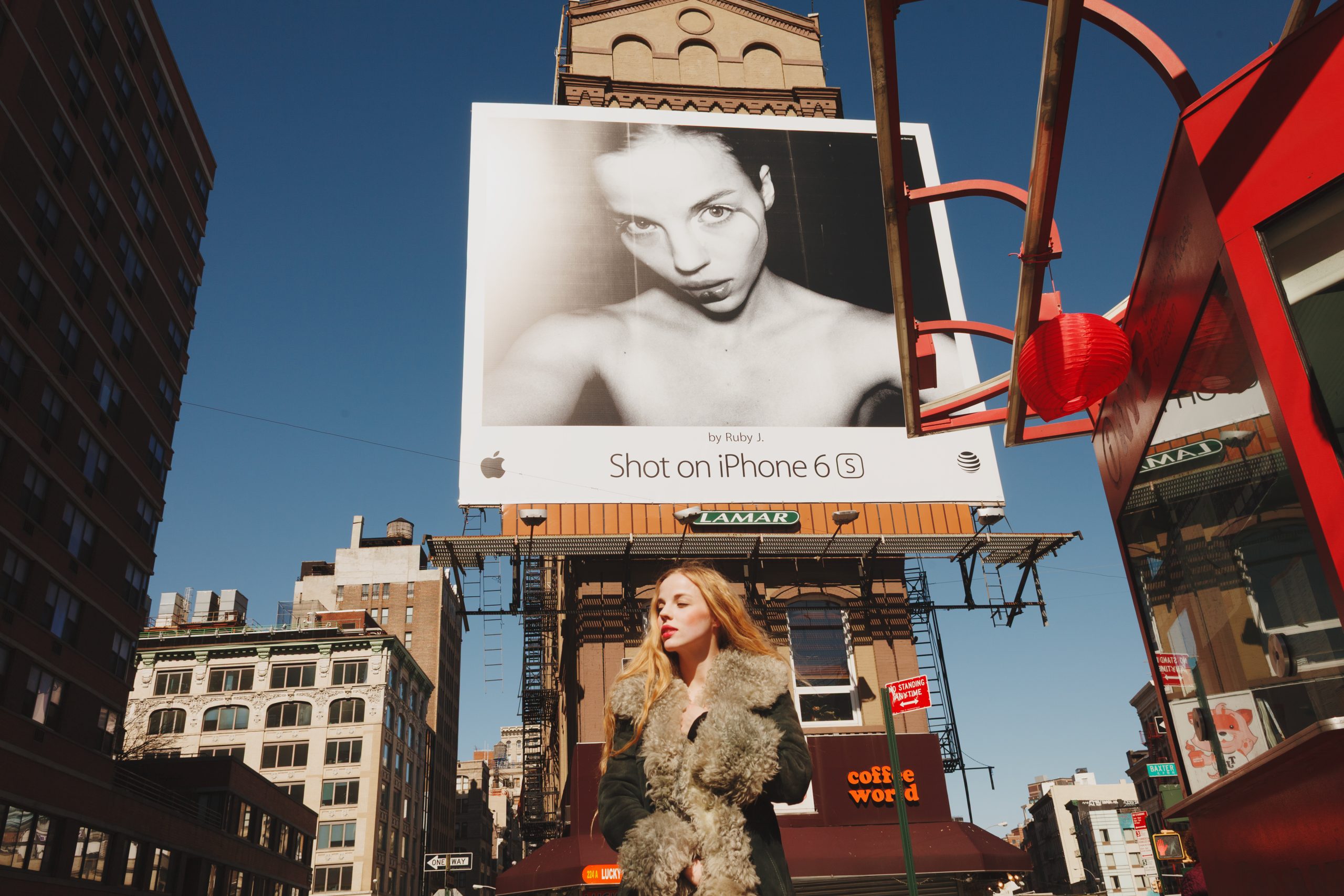 Ruby June beneath a large Apple Shot on iPhone billboard displaying her self-portrait in New York.